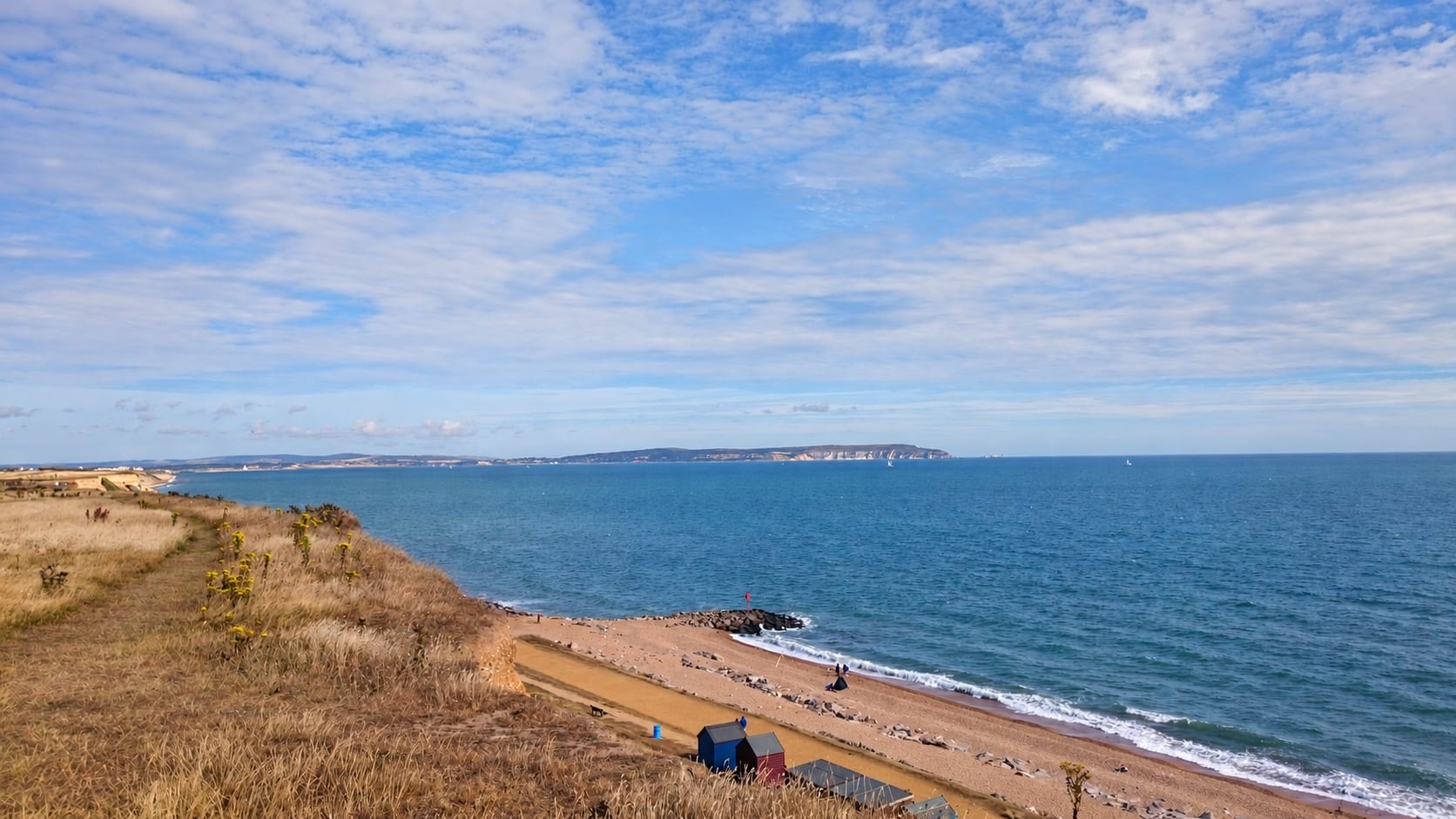 Christchurch Bay and the Isle of Wight, with beach huts and the beach below the cliff.