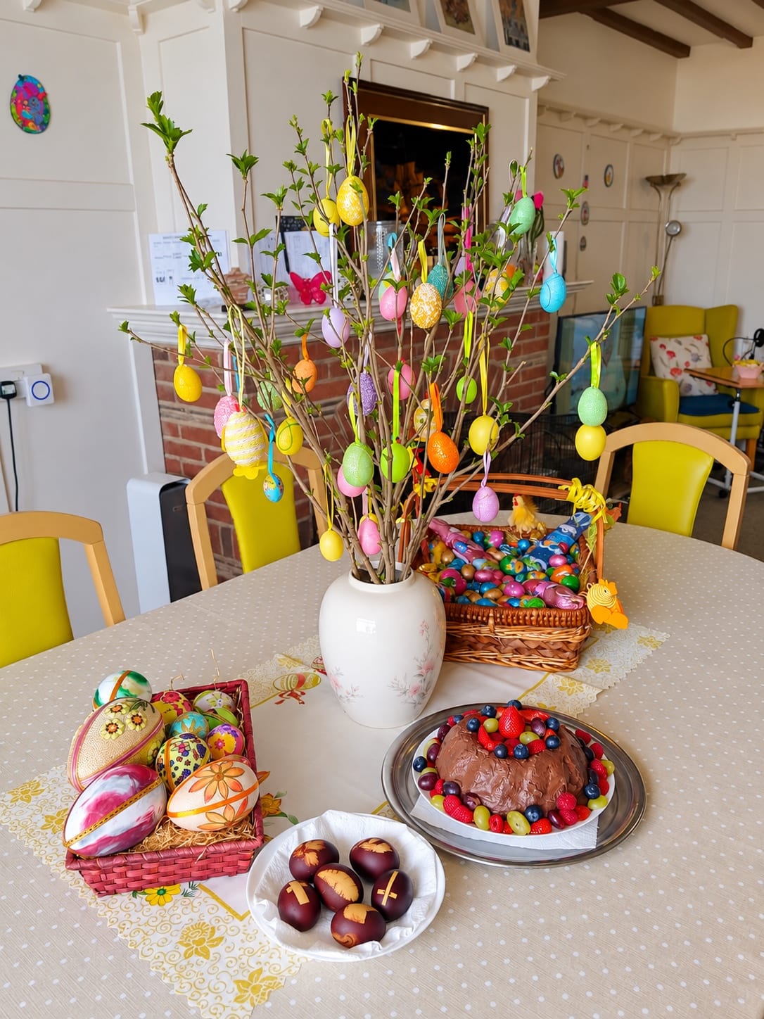 An Easter tree with painted eggs, baskets of chocolate eggs, and a chocolate cake with berries.