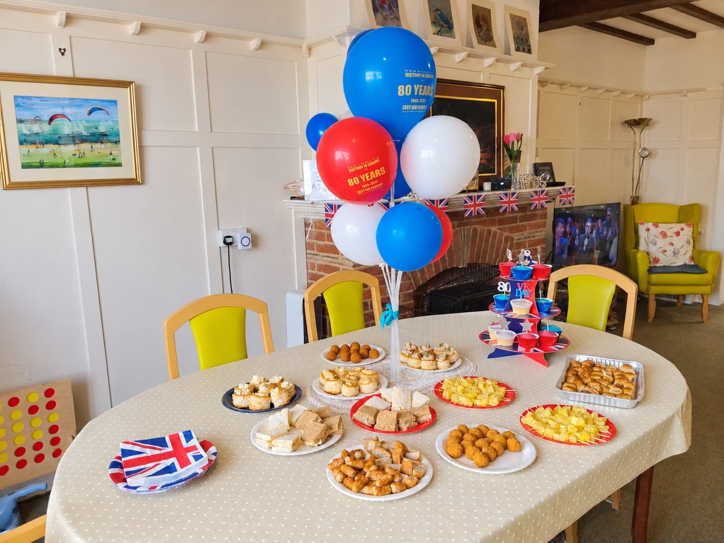 A VE Day table with sandwiches, cheese and pineapple, cupcakes, and red, white and blue balloons.