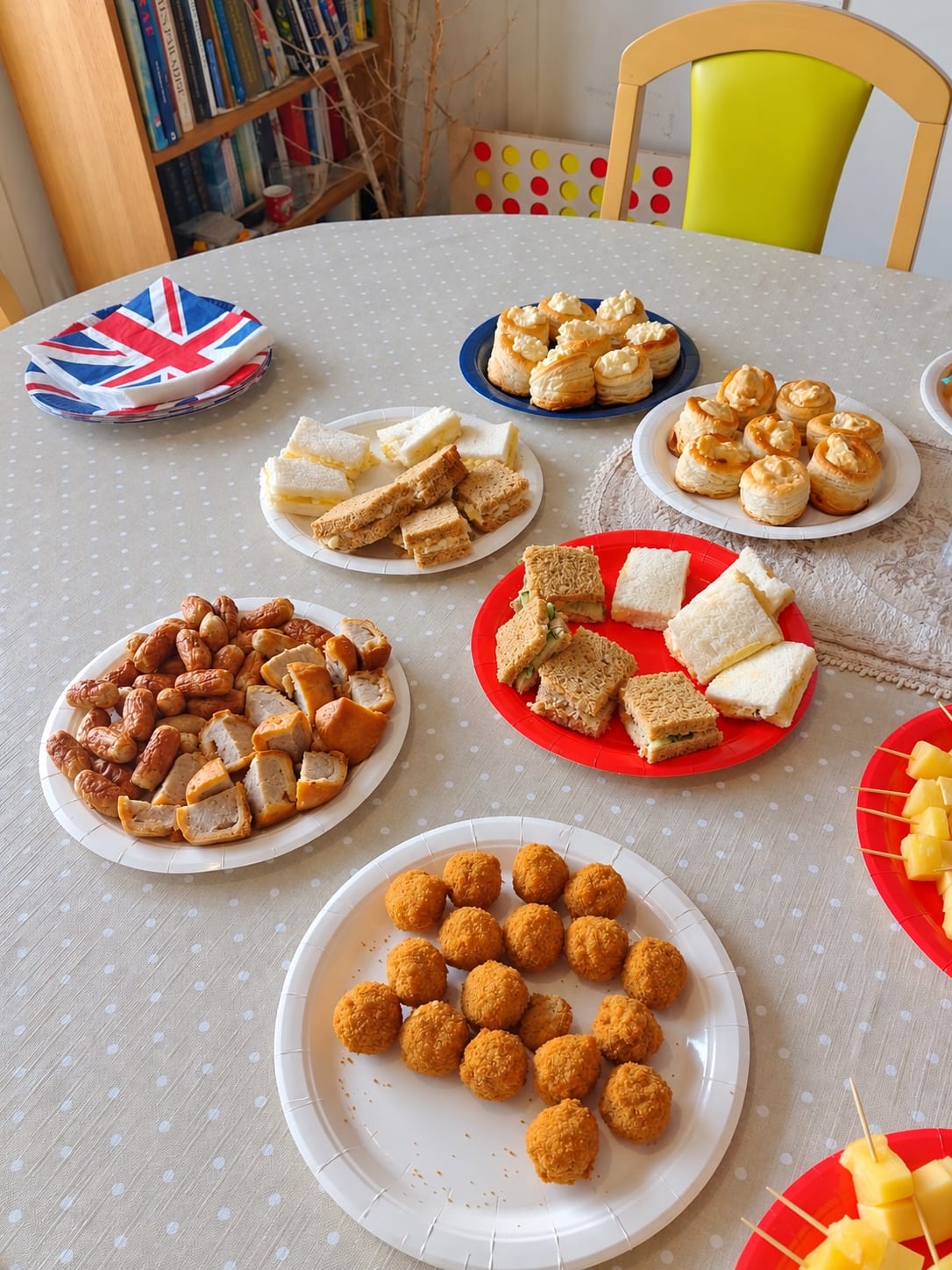 Plates of sandwiches, vol-au-vents, sausage rolls and croquettes on a spotted tablecloth.